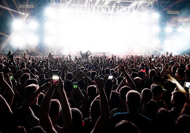 Back view of excited audience with arms raised cheering in front of the stage at music concert. Copy space.