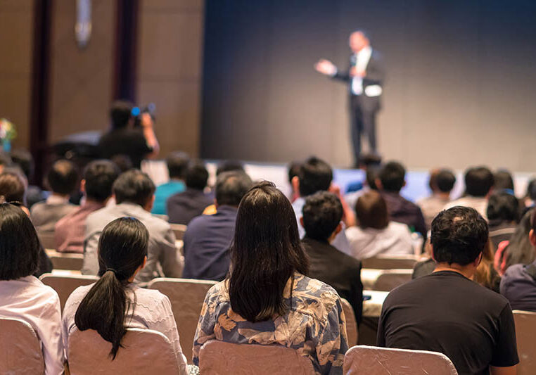 Rear side of Audiences sitting and listening the speackers on the stage in low light conference hall, event and seminar concept