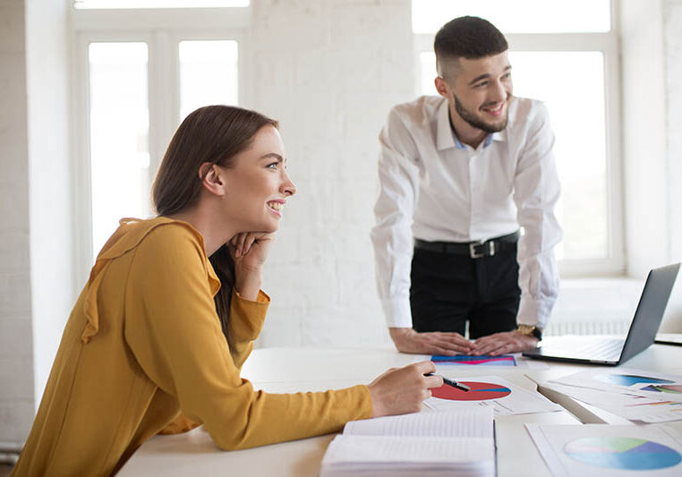 Young business man and woman happily looking aside working with diagrams together in modern office