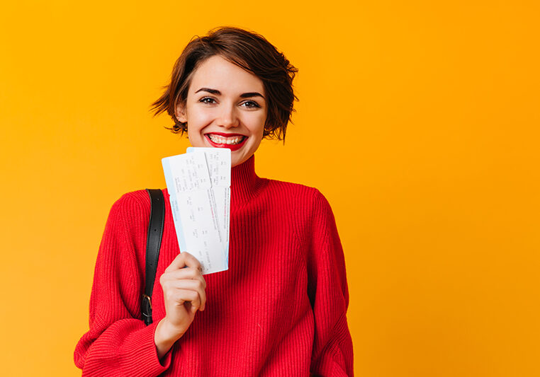 Cheerful girl with short hair holding tickets. European woman in red sweater waiting for travel.